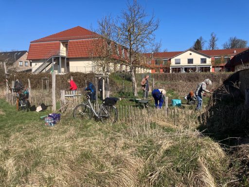 Personen arbeiten im Freien in einem bepflanzten Bereich bei sonnigem Wetter.
