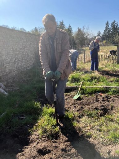 Eine Person gräbt mit einer Gartenspirale in einem sonnigen Gemüsebeet.