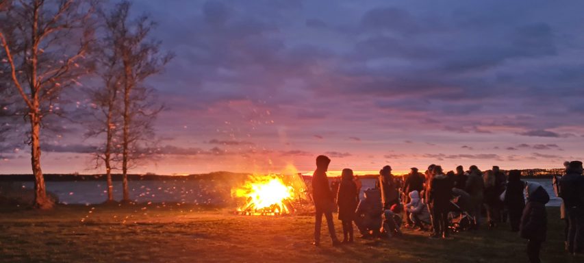 Gruppierung von Menschen am Lagerfeuer bei Sonnenuntergang am Rangsdorfer See.