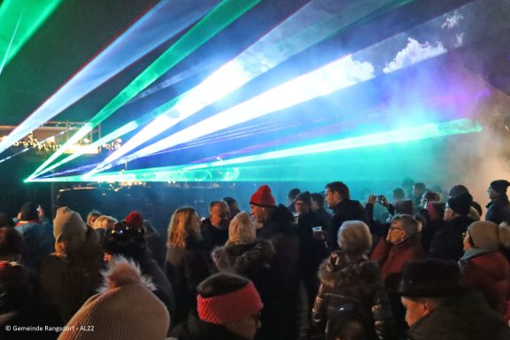 Farbenfrohe Lichtshow mit Laserstrahlen über einer Menschenmenge bei Nacht.