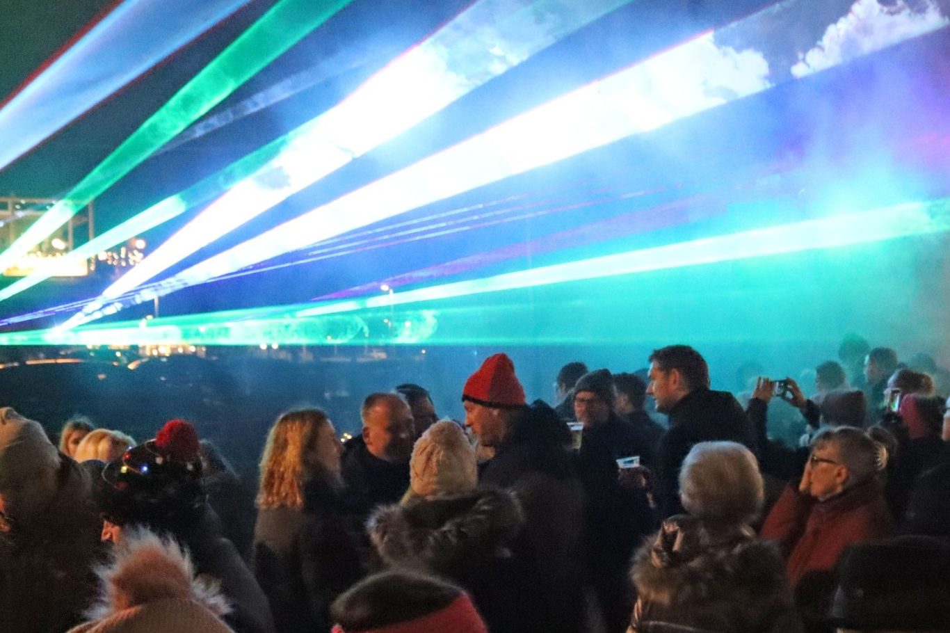 Menschenmengen bei einem Event mit bunten Lichtstrahlen im Hintergrund.