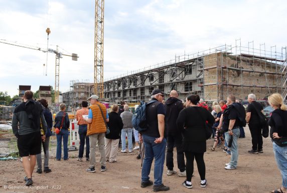 Menschen stehen vor einem Baustelle mit Kran und neuem Gebäude im Hintergrund.