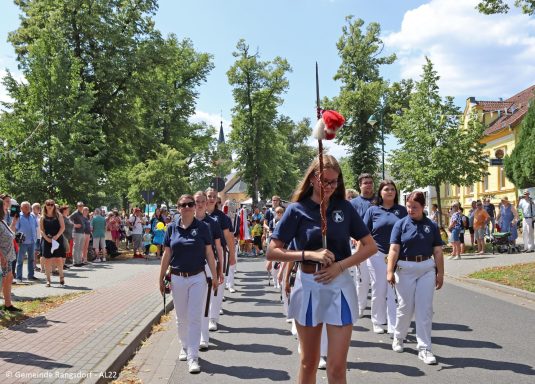 Eine Gruppe von Marschierern in Uniformen, begleitet von Zuschauern entlang der Straße.