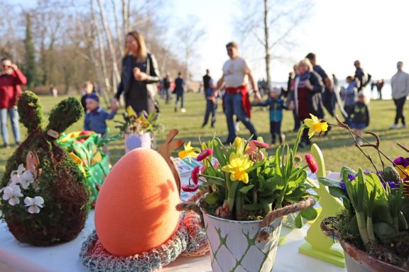 Frühlingsfest mit Menschen, bunten Blumen und Ostereiern im Vordergrund.