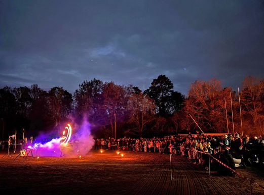 Osterfeuer mit bunten Lichtern und Menschenmenge bei Dämmerung im Freien.