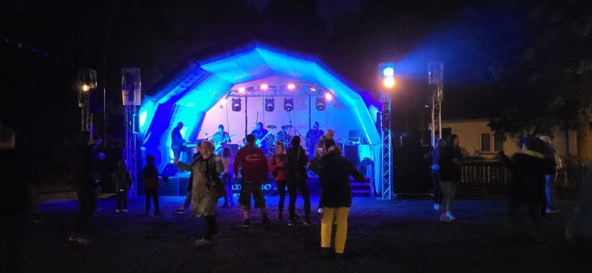 Menschen tanzen vor einer beleuchteten Bühne bei einer nächtlichen Veranstaltung.