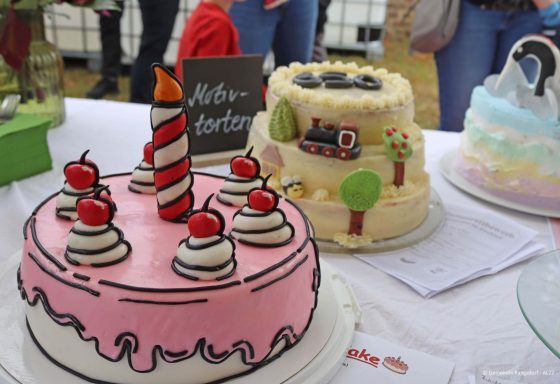 Zwei farbenfrohe Torten: eine rosa mit Kirschen und eine mit Bäumen und einem Zug.