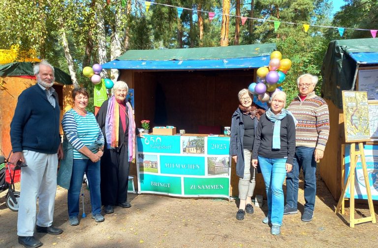 Vereinsmitglieder stehen vor einem Stand, geschmückt mit Ballons und bunten Plakaten.