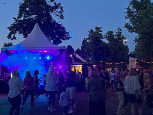 Menschenmenge bei einer Veranstaltung im Freien mit bunten Lichtern und Musikbühne.