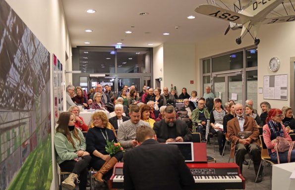 Eine große Menschengruppe sitzt beim Neujahrsempfang, während ein Musiker spielt.